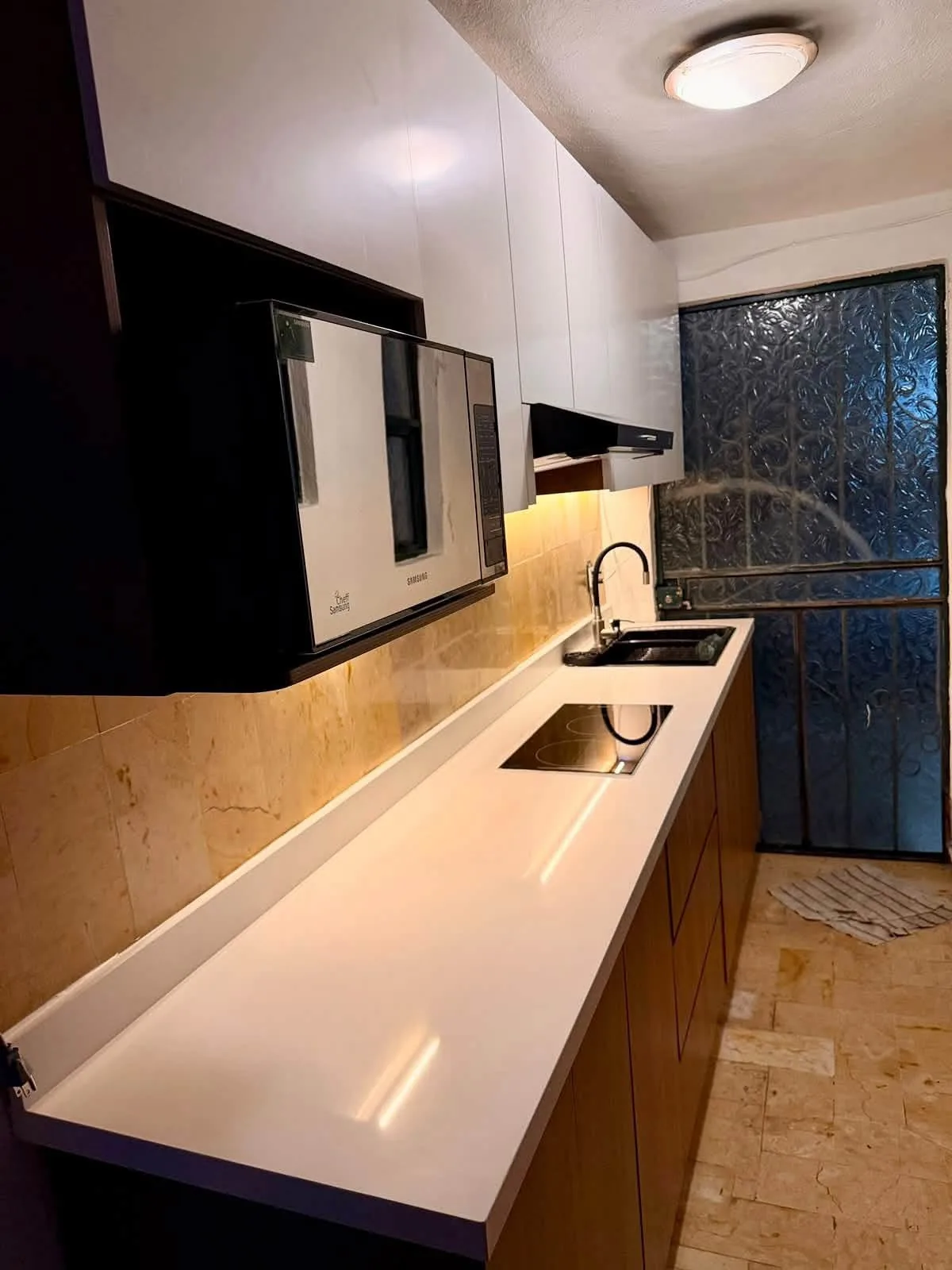 Cocina lineal con cubierta blanca y gabinetes de madera